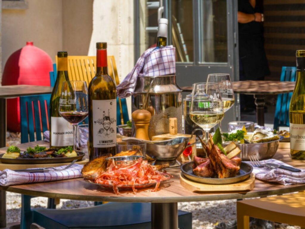 Table du restaurant la Basse-Cour à Lagrasse contenant du vin et des plats.